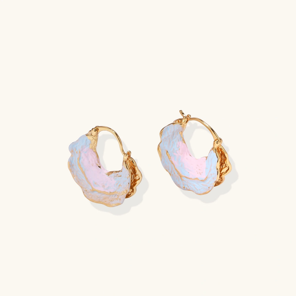 Shell-shaped hoop earrings with iridescent blue-pink enamel and gold trim on cream background