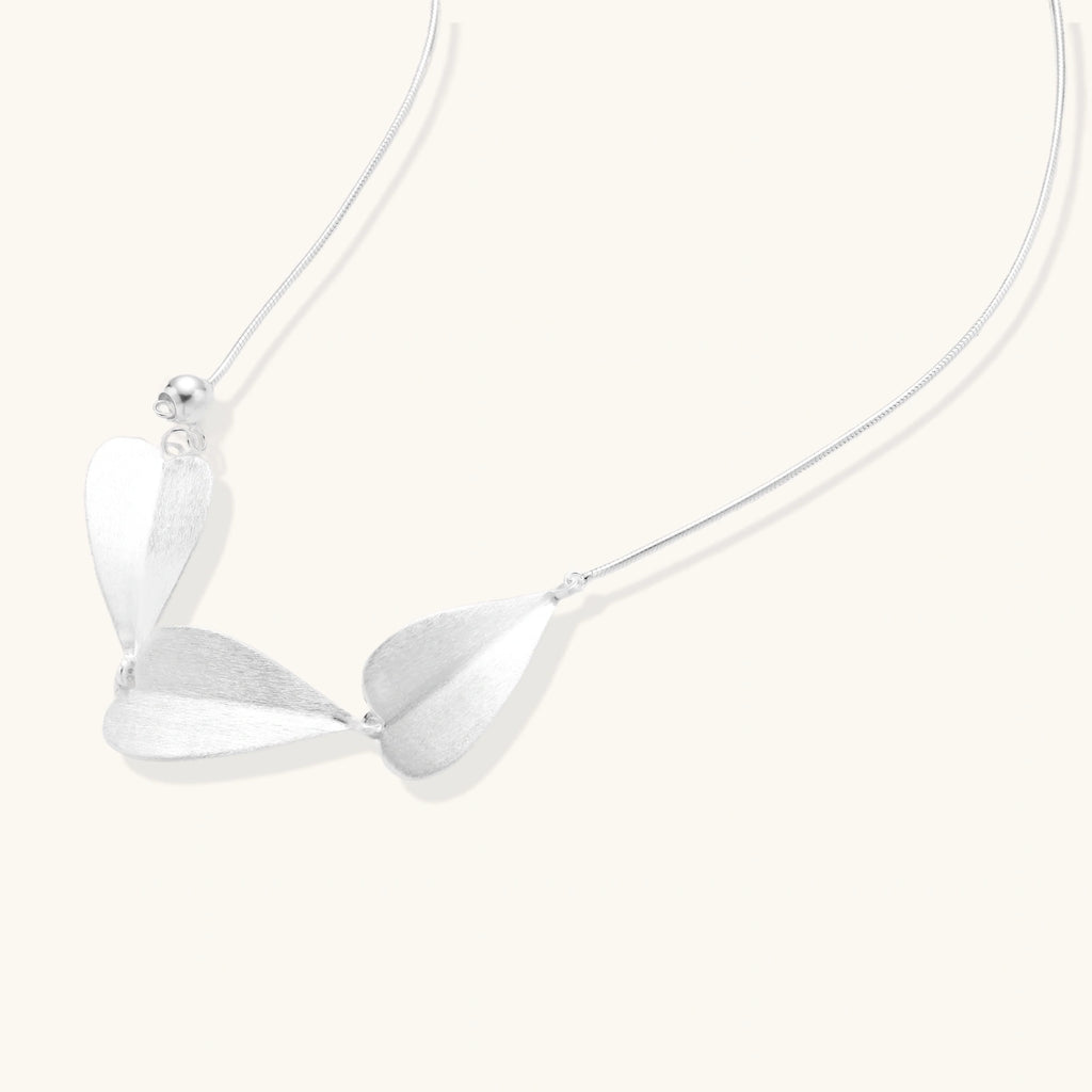 Minimalist sterling silver necklace with three brushed leaf-shaped pendants on delicate chain against white background