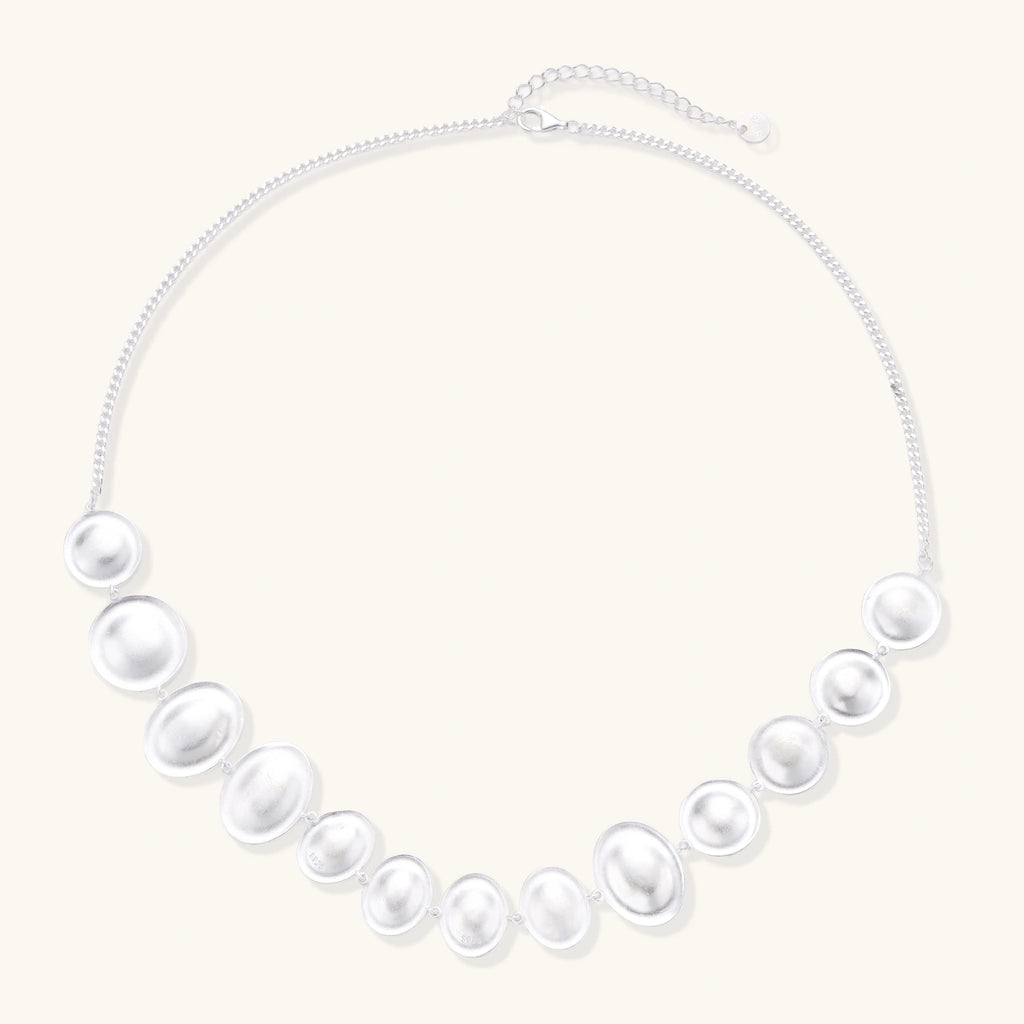 Graduated pearl-finish silver discs forming an organic bubble bib necklace on delicate chain against cream background.