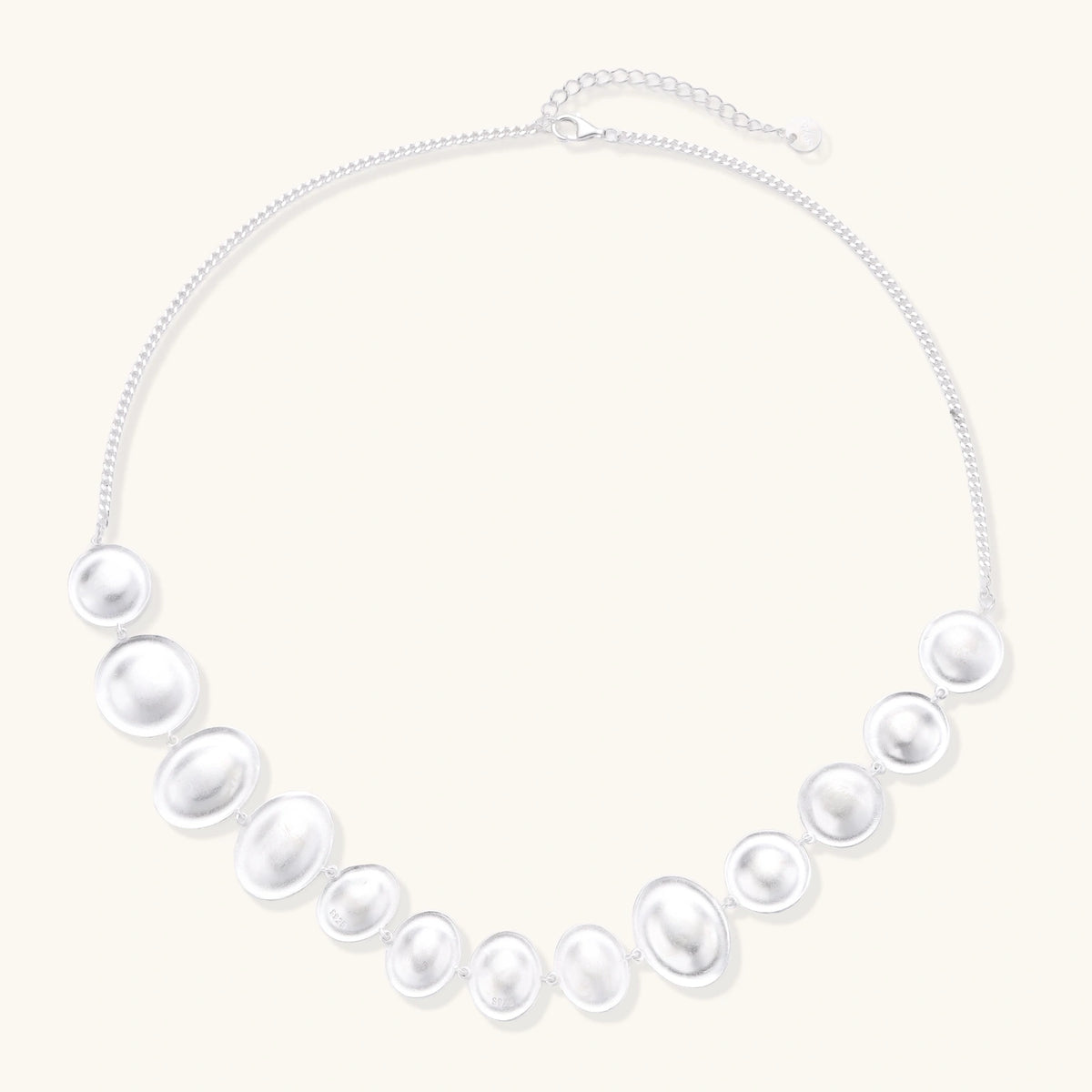 Graduated pearl-finish silver discs forming an organic bubble bib necklace on delicate chain against cream background.