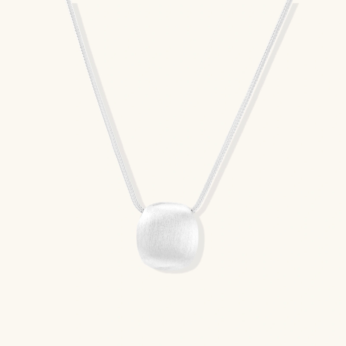 Minimalist brushed sterling silver dome pendant on delicate chain against cream background, showing matte textured finish