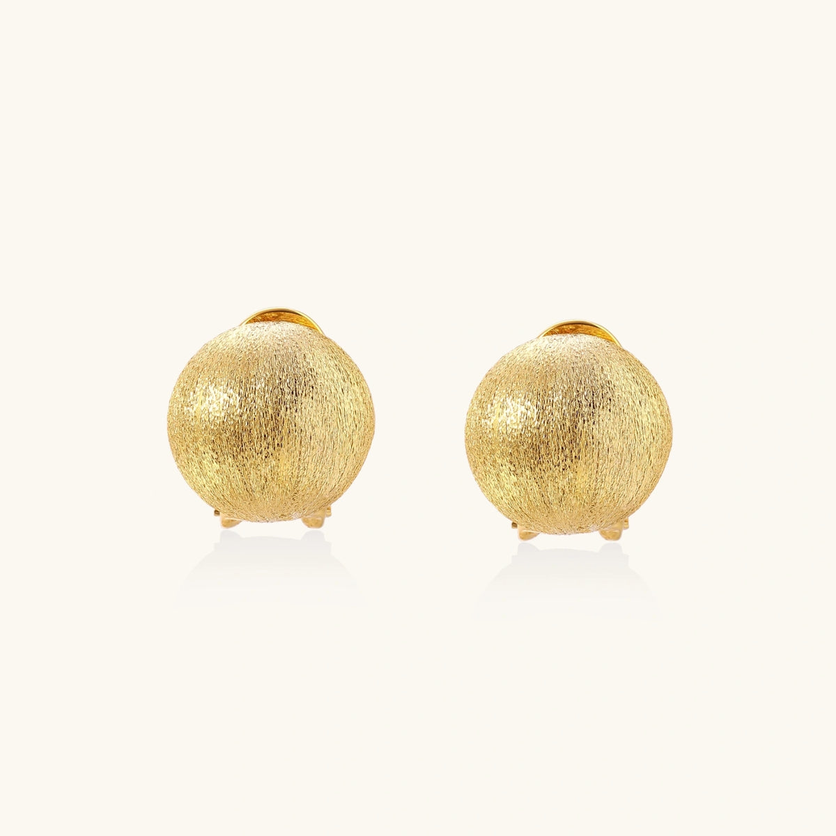 Pair of brushed gold dome earrings with clip backs showing textured matte finish on cream background