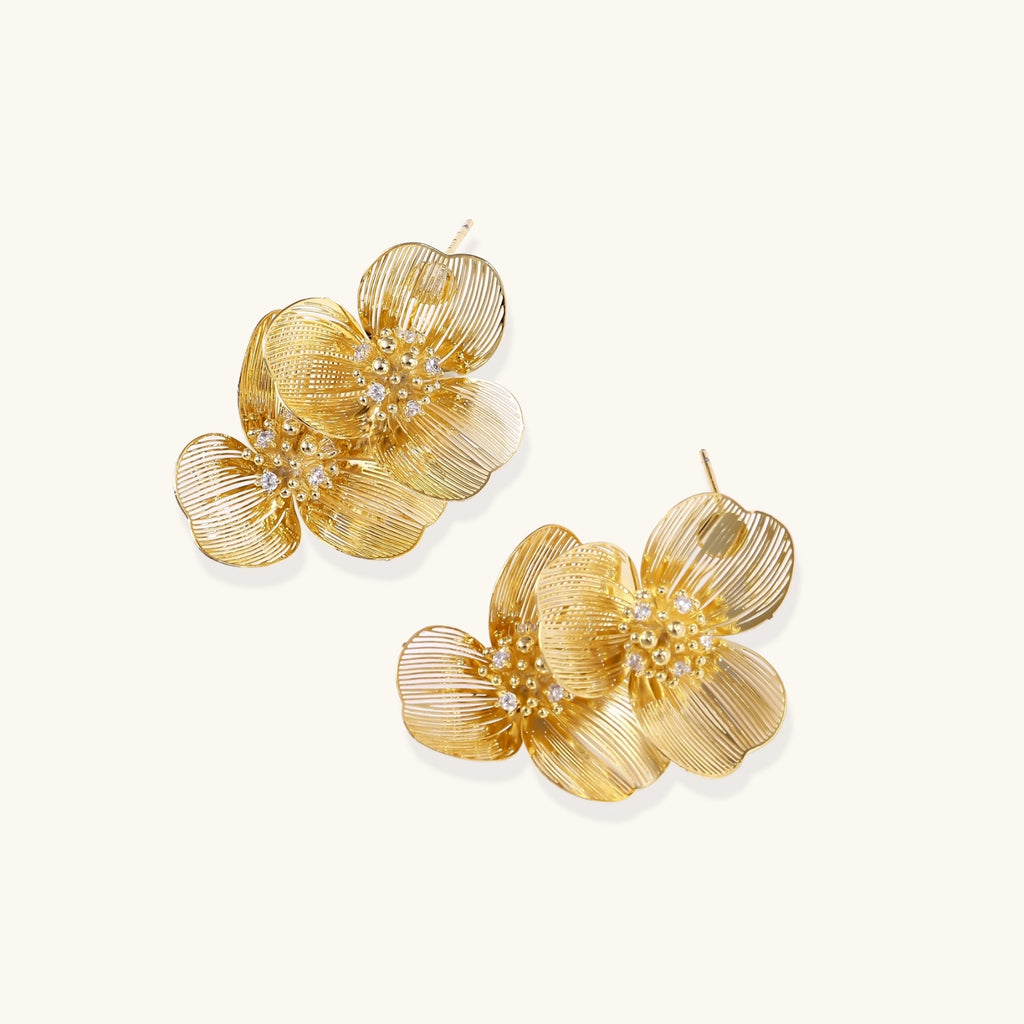 Pair of gold-plated double flower earrings with textured petals and crystal centers on cream background.