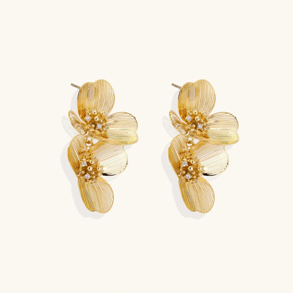 Pair of gold-plated double flower earrings with textured petals and crystal centers on cream background.