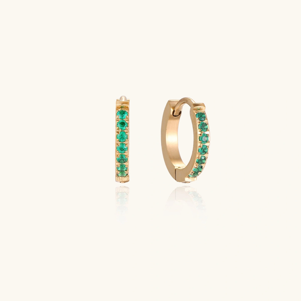 Pair of small gold huggie hoop earrings with bright green cubic zirconia stones on cream background