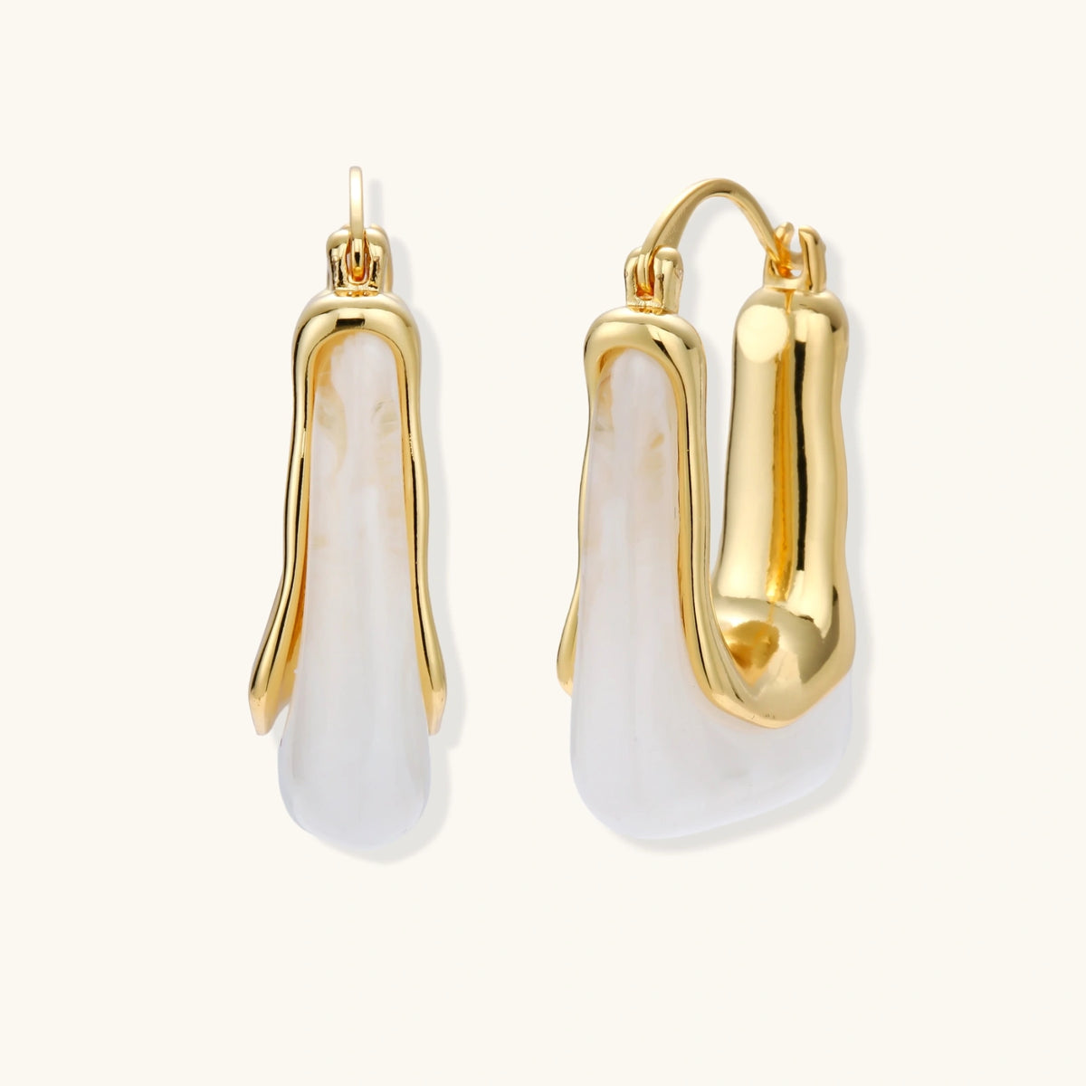 Sculptural gold-plated hoop earrings with flowing curved design and lever-back closure on cream background.
