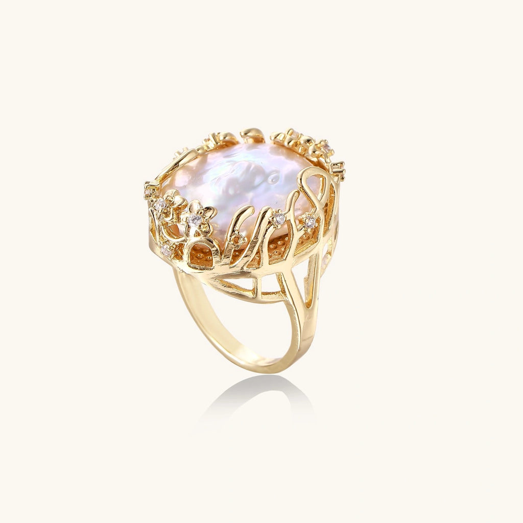 Gold filigree crown ring cradling an iridescent baroque freshwater pearl with crystal accents on white background