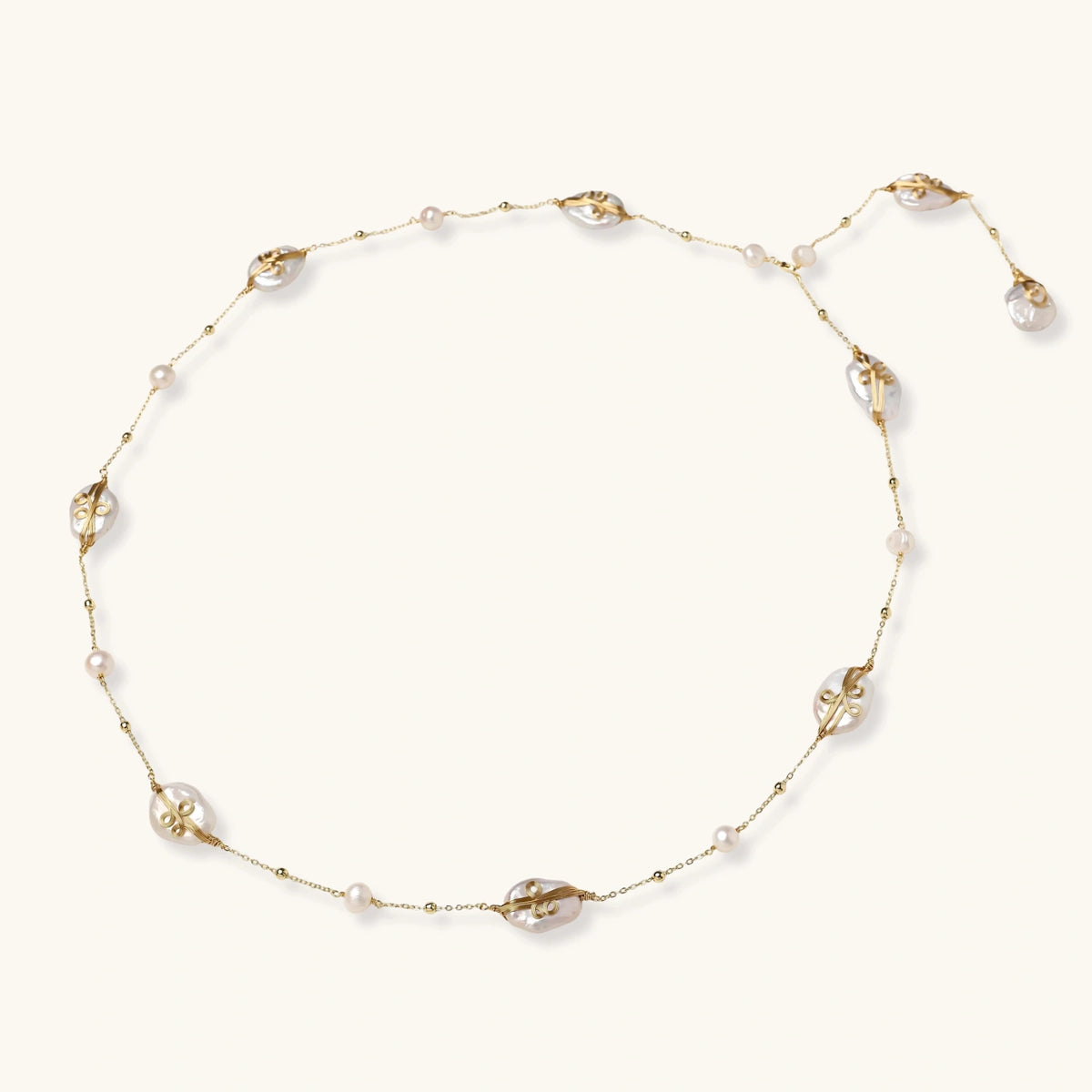 Long gold chain necklace with baroque pearls wrapped in leaf designs and small freshwater pearls spaced along the strand