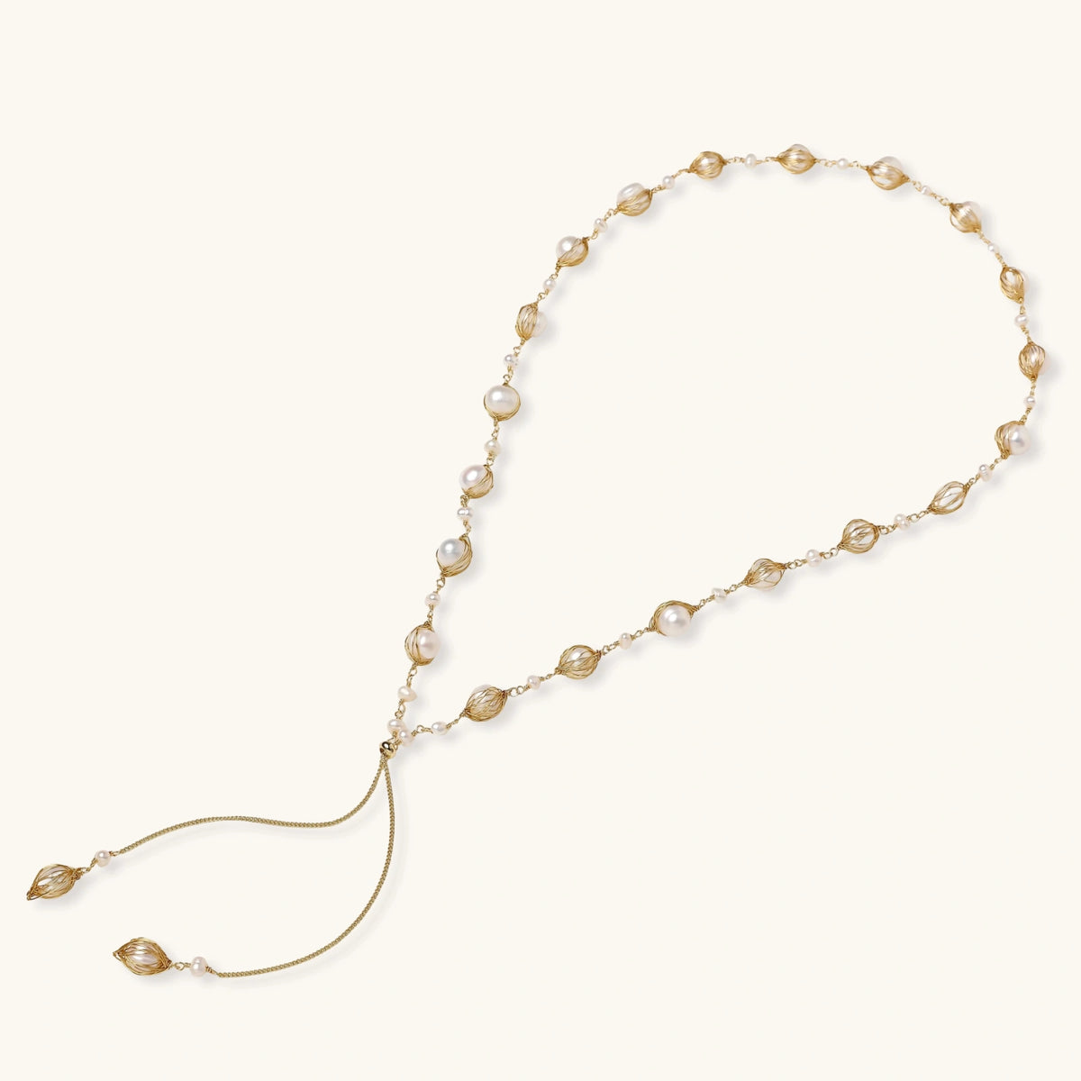 Adjustable gold lariat necklace with freshwater pearls nested in delicate cage settings and Y-shaped tassel drop